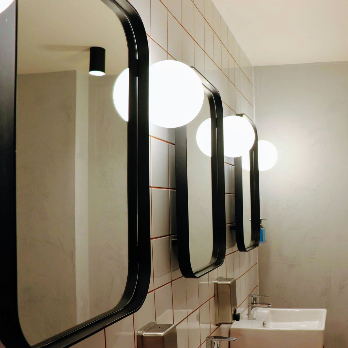 Three bathroom mirrors lined up on the wall with a wall light in between each mirror.