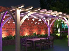 A pergola with outdoor lights installed inside a yard with tall brick walls.