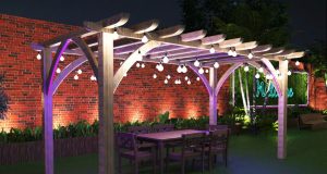 A pergola with outdoor lights installed inside a yard with tall brick walls.