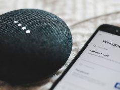 A smartphone beside a Google Home Mini speaker.