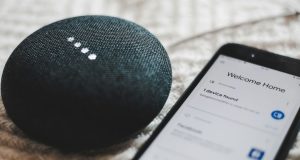 A smartphone beside a Google Home Mini speaker.