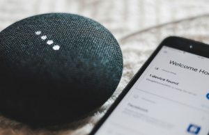 A smartphone beside a Google Home Mini speaker.