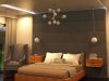 A modern bedroom washed in warm lighting from recessed ceiling lights and strip lights, a statement pendant light is hanging in the middle.