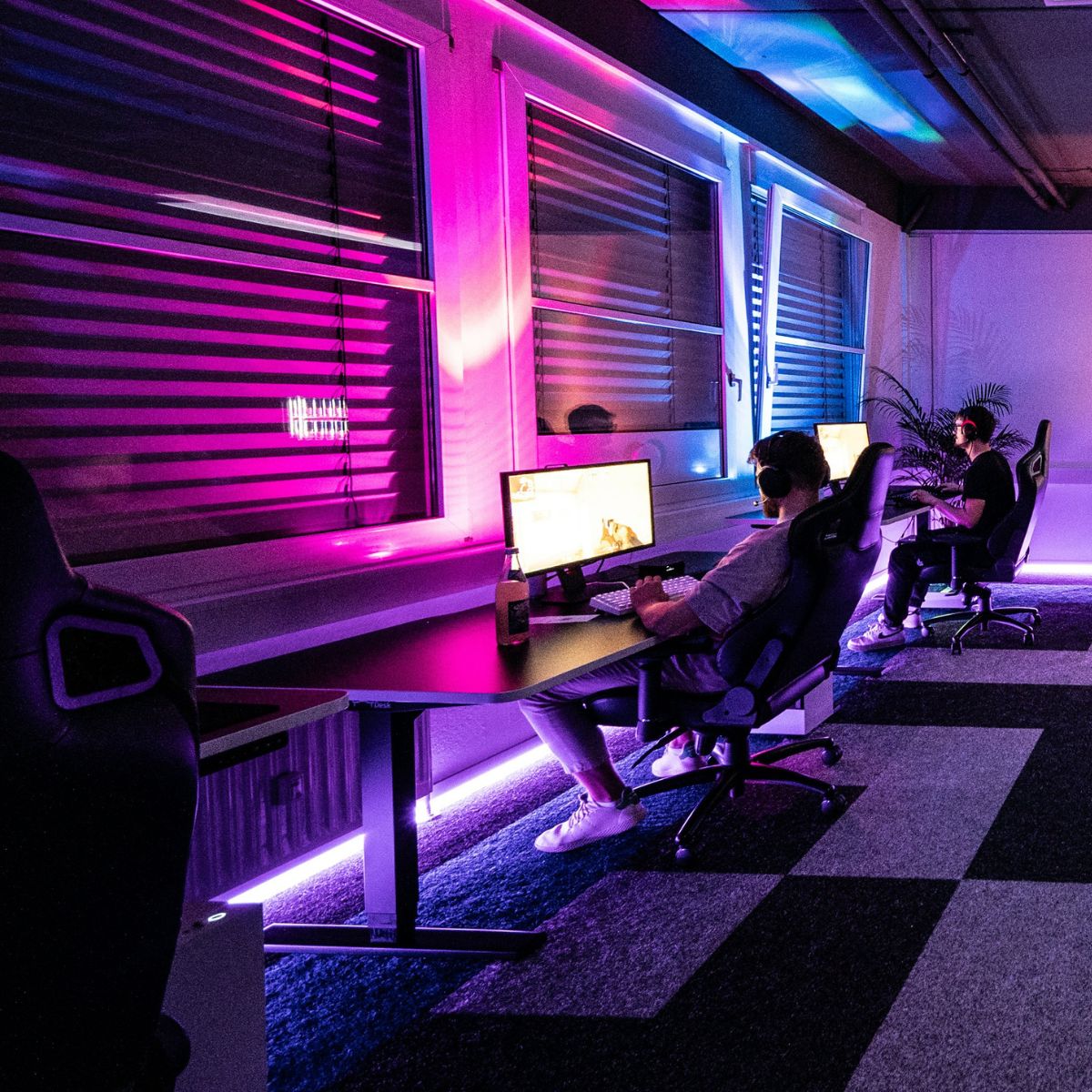 A gaming room with pink and blue lighting on the wall, and a purple light on the floor.