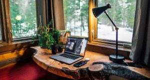 A wooden desk stationed by the window with a desk lamp glowing with warm light beside it.