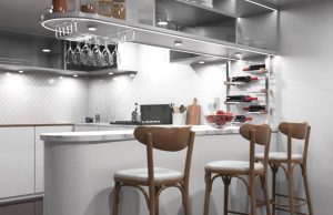 Kitchen Lighting Ideas for Cooking, Dining, and Entertaining A modern kitchen with an island/bar area and bar stools, under-cabinet lights are illuminating the space.
