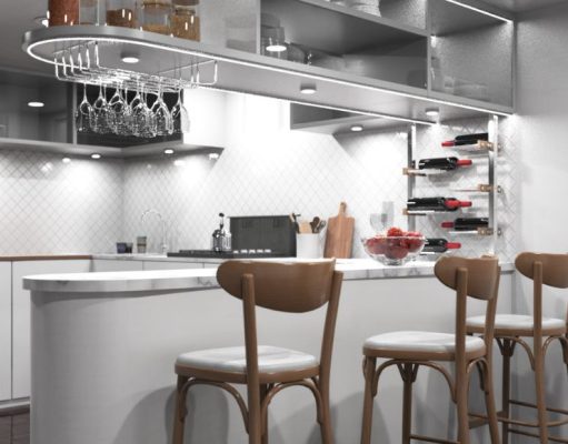 A modern kitchen with an island/bar area and bar stools, under-cabinet lights are illuminating the space.
