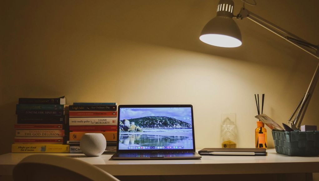 A home office desk illuminated by a single desk lamp with warm white tone.