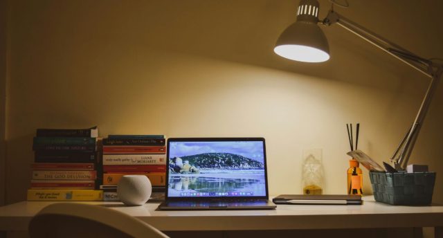 A home office desk illuminated by a single desk lamp with warm white tone.