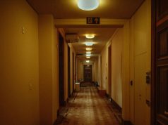 A residential building hallway with warm lighting and a visible emergency exit sign on one of the beams.