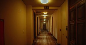 A residential building hallway with warm lighting and a visible emergency exit sign on one of the beams.