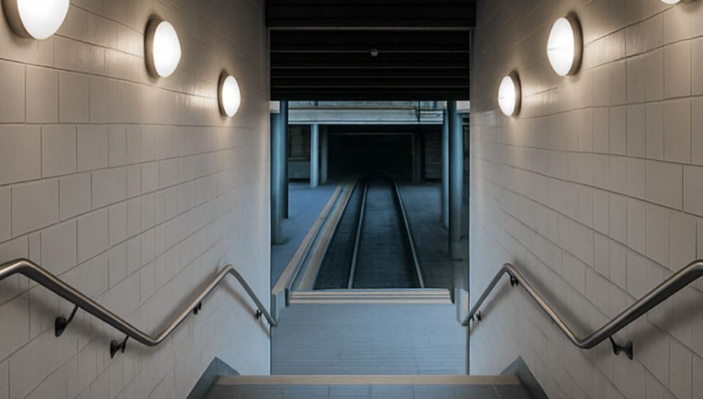 A stairwell going down with multiple round bulkhead lights on both sides.