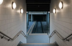 Emergency Lighting Testing Requirements A stairwell going down with multiple round bulkhead lights on both sides.