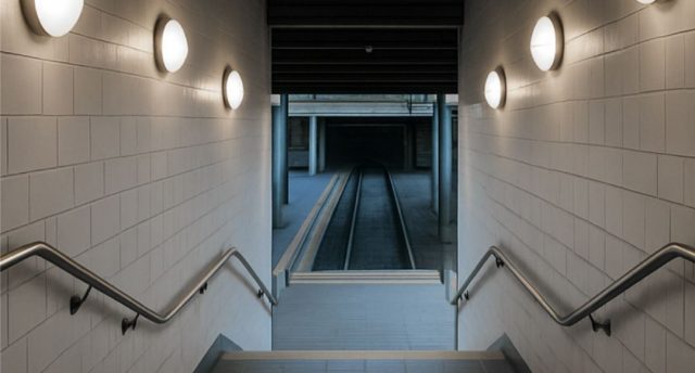 A stairwell going down with multiple round bulkhead lights on both sides.