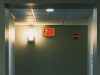 A corridor wall with a red EXIT sign beside a wall light with a warm glow.