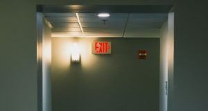 A corridor wall with a red EXIT sign beside a wall light with a warm glow.