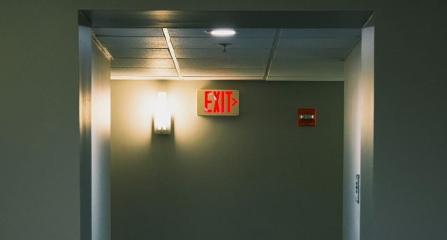 A corridor wall with a red EXIT sign beside a wall light with a warm glow.