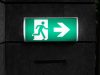 Exit Sign Placement Rules & Best Practices A green emergency exit signage with backlighting in a dark corridor.