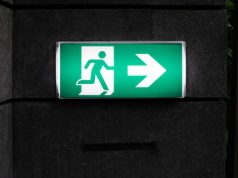 A green emergency exit signage with backlighting in a dark corridor.