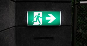 A green emergency exit signage with backlighting in a dark corridor.