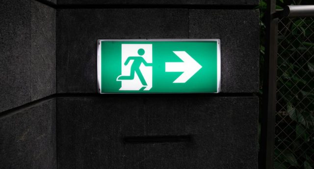A green emergency exit signage with backlighting in a dark corridor.