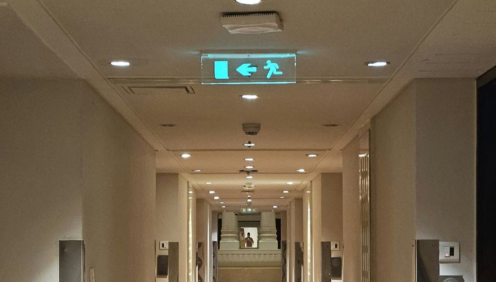 A building corridor with a glowing emergency exit sign in the ceiling.