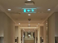 A building corridor with a glowing emergency exit sign in the ceiling.