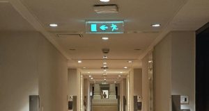 A building corridor with a glowing emergency exit sign in the ceiling.