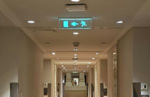 A building corridor with a glowing emergency exit sign in the ceiling.