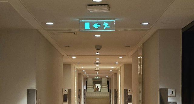 A building corridor with a glowing emergency exit sign in the ceiling.