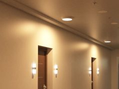 A hallway with multiple doors illuminated by round bulkhead lights on the ceiling and wall lights on both sides of each door.