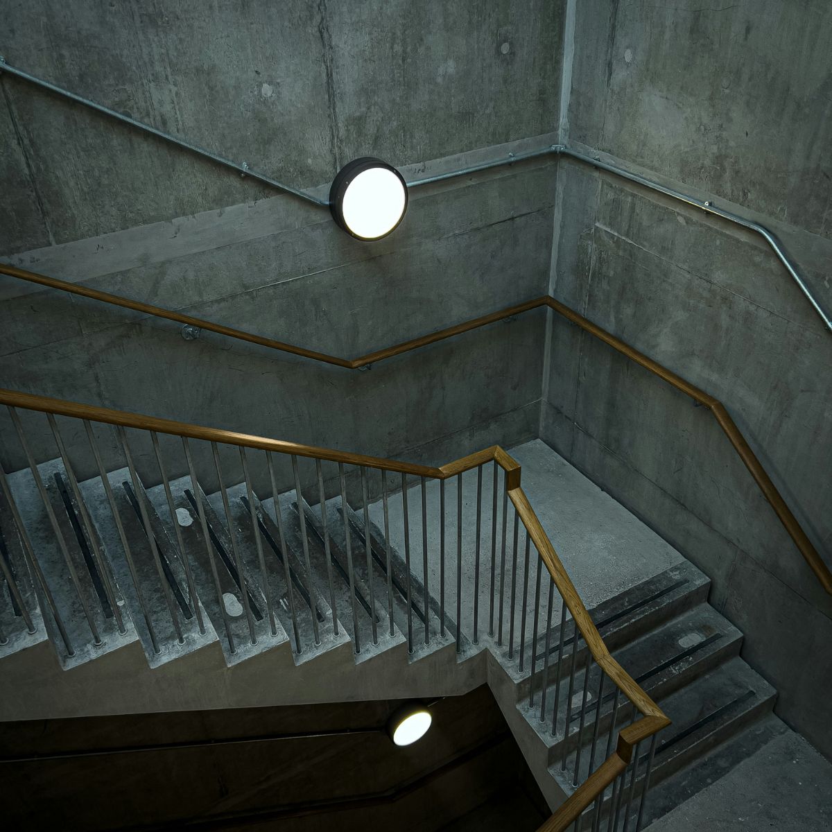 A concrete staircase used as a fire exit in a building with a single round bulkhead light on each level.