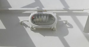 A bullhead installed on a wall just below a pipe, painted white as the wall.