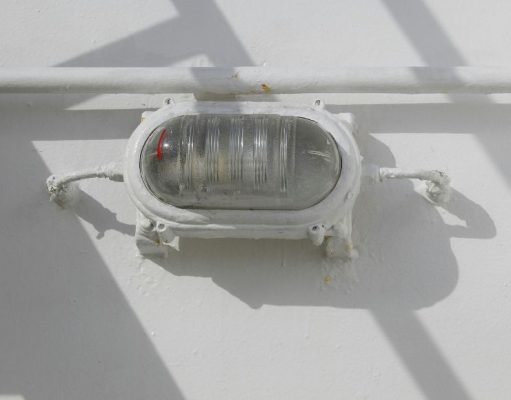 A bullhead installed on a wall just below a pipe, painted white as the wall.