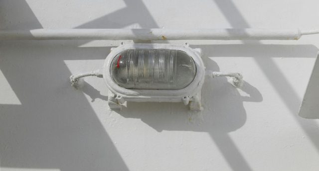 A bullhead installed on a wall just below a pipe, painted white as the wall.