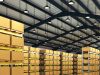 High Bay LED Lighting: How to Choose the Right Solution for Your Warehouse A warehouse with multiple boxes on racks and multiple high bay lights hanging from the ceiling.