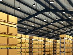 High Bay LED Lighting: How to Choose the Right Solution for Your Warehouse A warehouse with multiple boxes on racks and multiple high bay lights hanging from the ceiling.