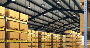 A warehouse with multiple boxes on racks and multiple high bay lights hanging from the ceiling.