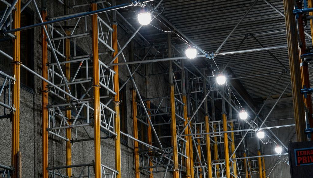 A series of big, bright lights installed along steel beams inside a warehouse.