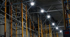 A series of big, bright lights installed along steel beams inside a warehouse.