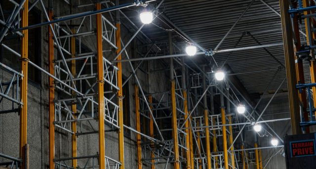 A series of big, bright lights installed along steel beams inside a warehouse.