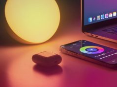 A warm light, airpods, laptop, and phone with colour controls for the light on a desk.