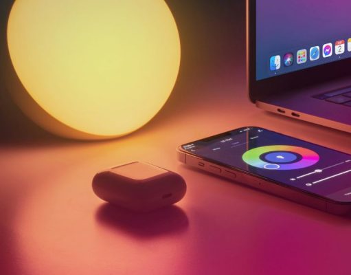 A warm light, airpods, laptop, and phone with colour controls for the light on a desk.