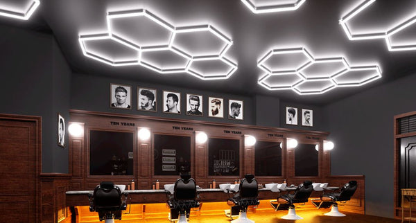 A modern barber shop with dark walls and ceiling, illuminated by multiple hexagonal lighting systems installed on the ceiling.