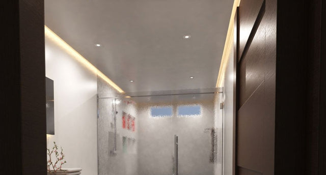 A view from the door of a modern bathroom showcasing its warm LED strip lighting along the ceiling.