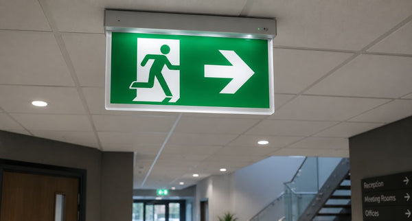 A green emergency exit sign installed in the middle of a commercial building hallway.