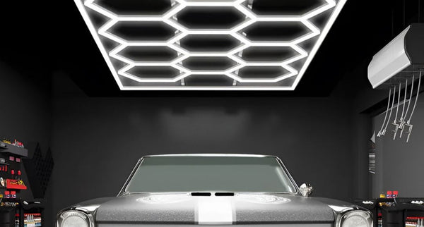 A modern garage with black walls and ceiling, a project car at the centre, and above it is a honeycomb LED light setup.