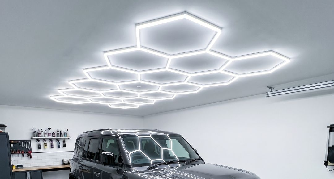 A bright modern home garage with a full set of hexagon lighting installed on the ceiling above the parked shiny grey car.