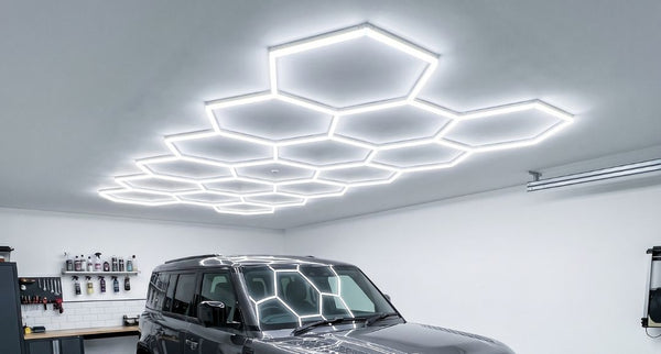 A bright modern home garage with a full set of hexagon lighting installed on the ceiling above the parked shiny grey car.