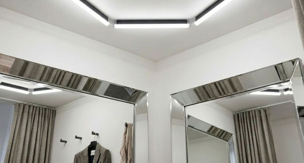 A small fitting room with mirrors and a bright set of ceiling lights.